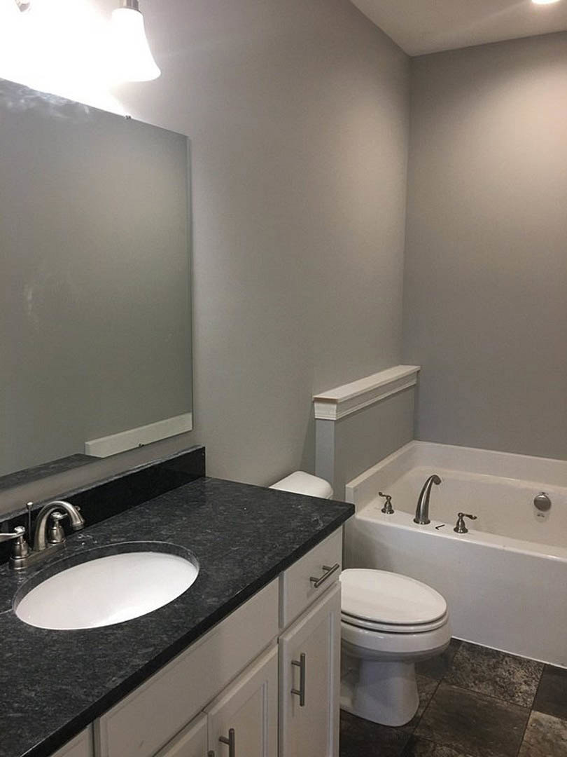 Modern bathroom featuring a freestanding white bathtub, rectangular sink with chrome faucet on a stone countertop, white toilet, light gray tile walls, and minimalistic fixtures.
