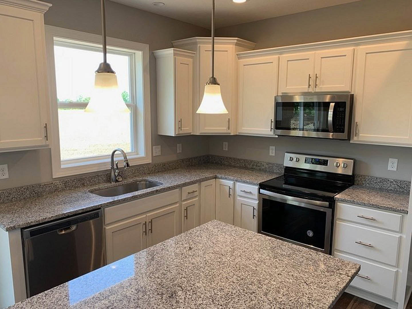 Granite countertops with white speckled surface, stainless steel sink, wood cabinetry, built-in microwave, black-door stove, dishwasher, and kitchen utensils including a ladle