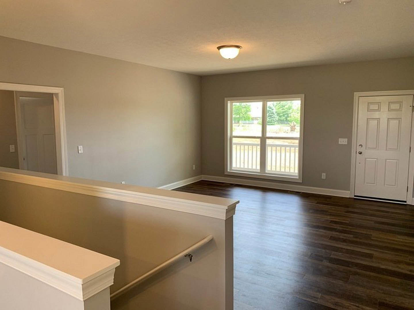 White door with silver handle beside window with white railing, hardwood flooring, light fixture on ceiling, neutral walls, modern interior finishes