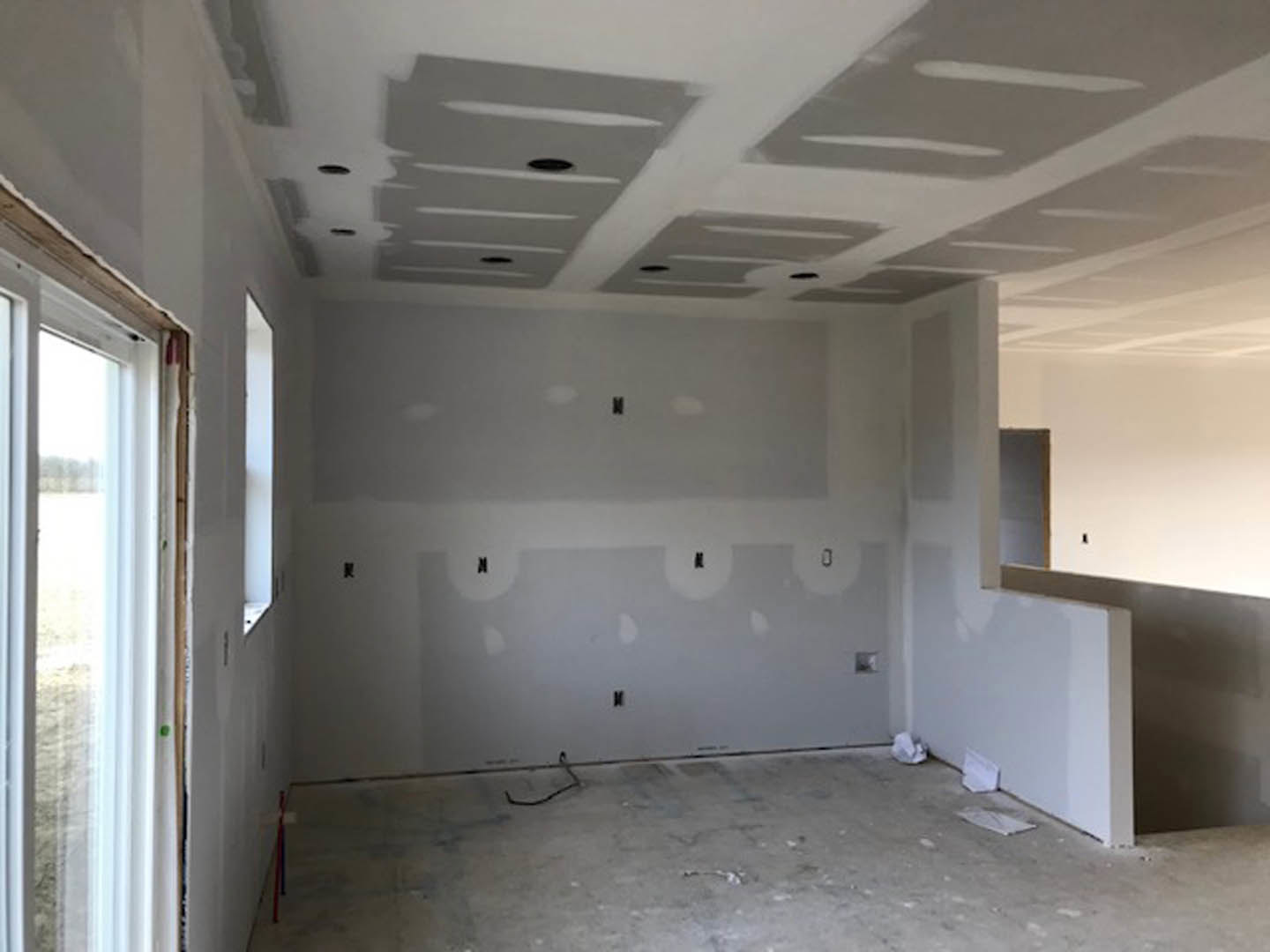 Bright room with smooth white plaster walls, large window with white trim, unfinished concrete floor, ceiling and wall featuring recessed holes for fixtures