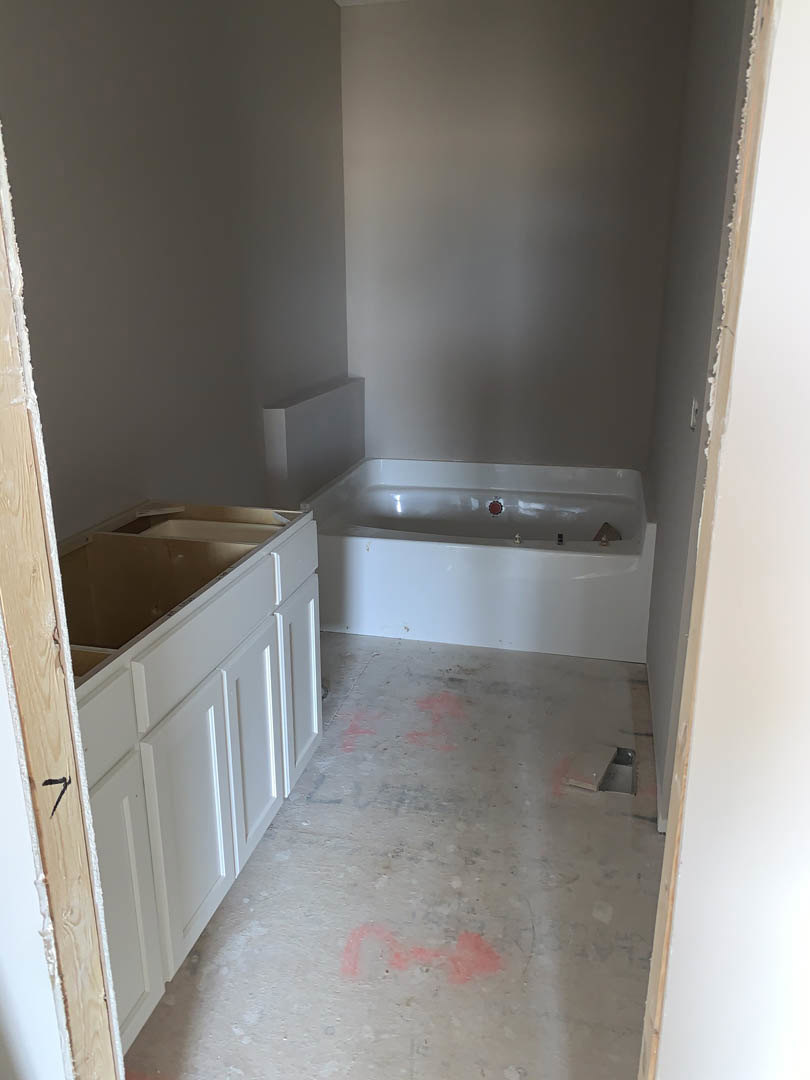 Bathroom with white freestanding bathtub, rectangular sink on vanity, light tile flooring, plaster walls, and open white cabinet drawers