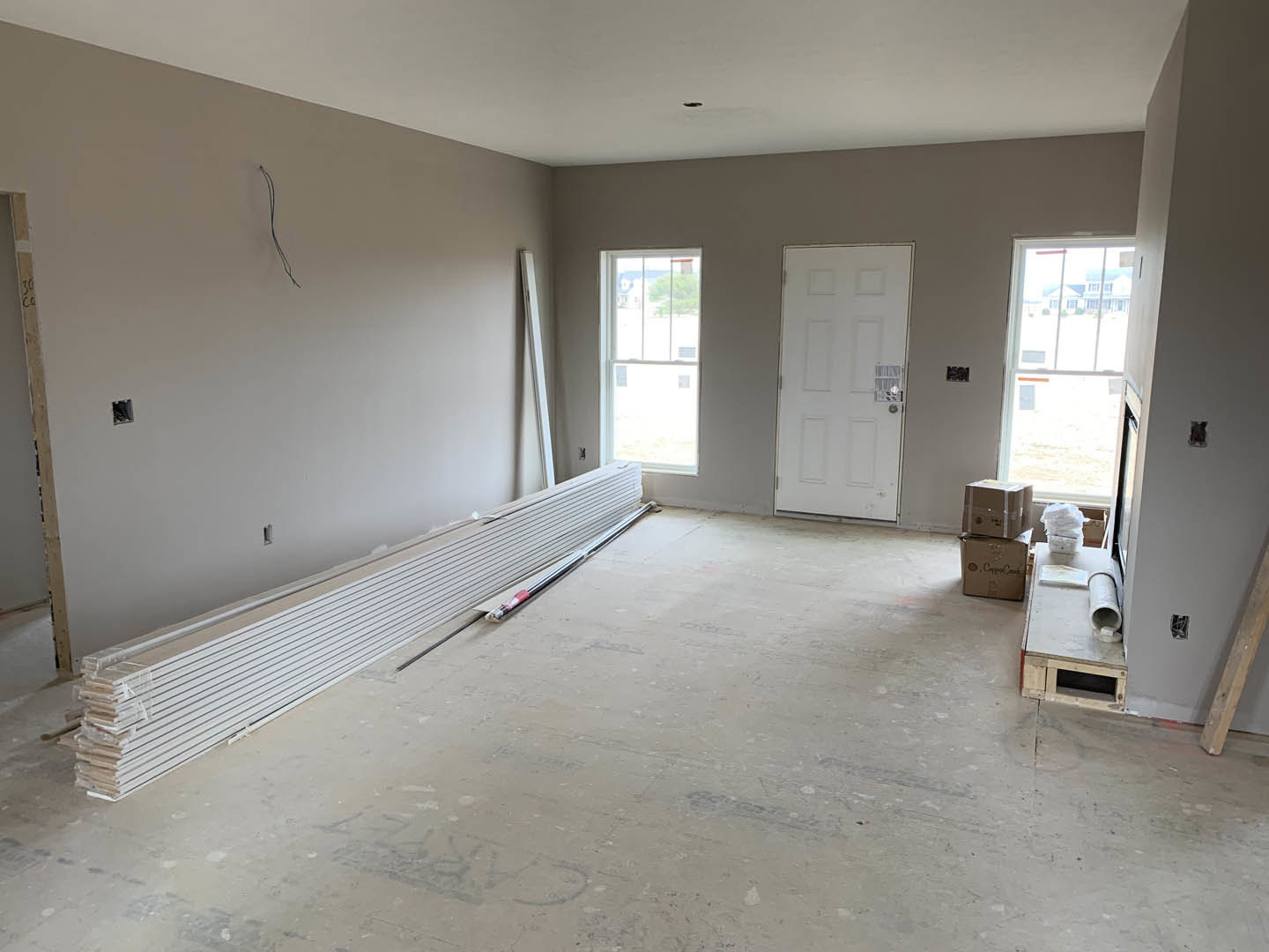 Bright room with plaster walls, light flooring, white-framed window, white door with matching handle, stacked white metal beams, wood pallet, and folded white towels.
