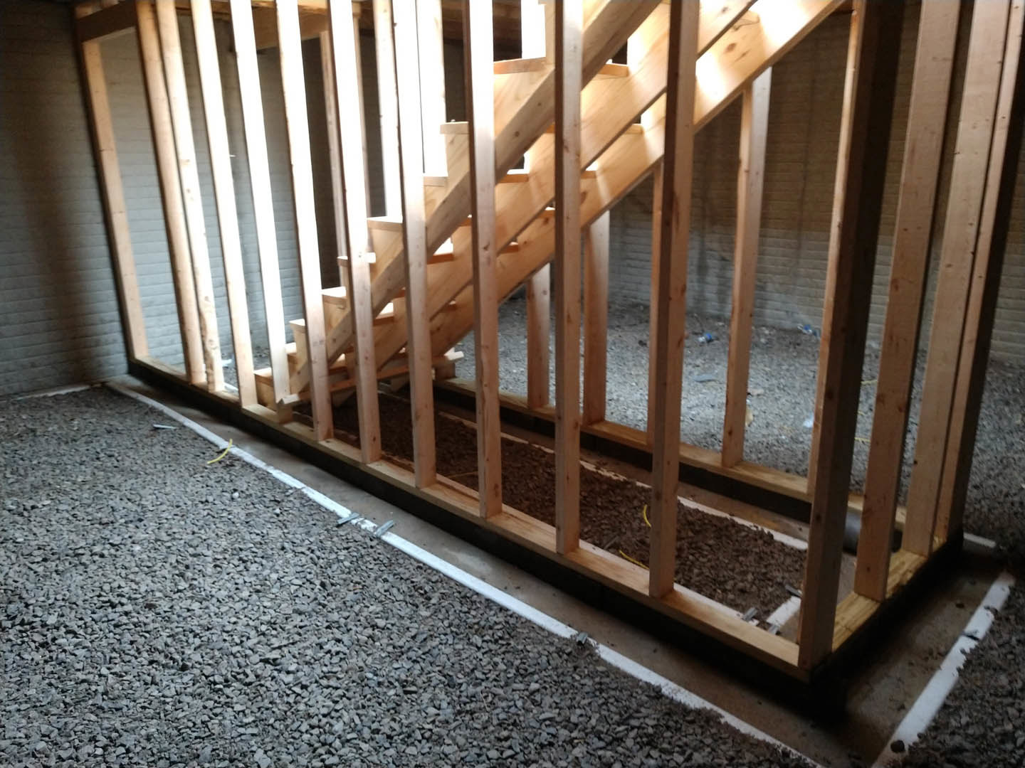 Wooden staircase with hardwood steps and handrail, yellow object on floor near wood-framed gravel area, white trim along wall, plank flooring throughout room