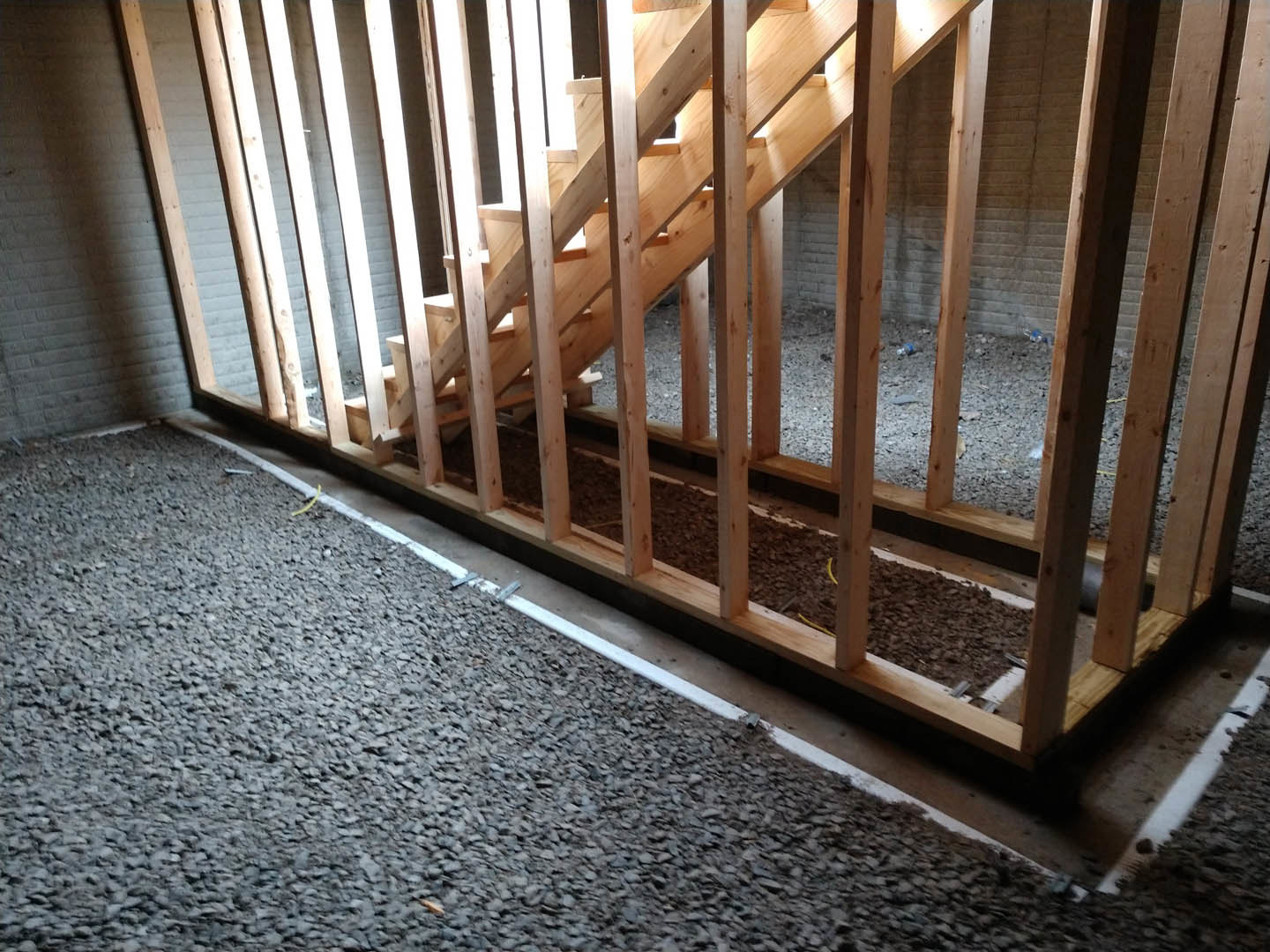 Wooden staircase with plank steps and handrail, hardwood flooring, wood-framed wall, yellow tube lying on the ground.