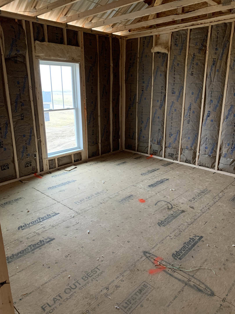 Unfinished room with exposed wooden ceiling beams, two windows, red paint markings on subfloor, plaster walls, and construction materials visible