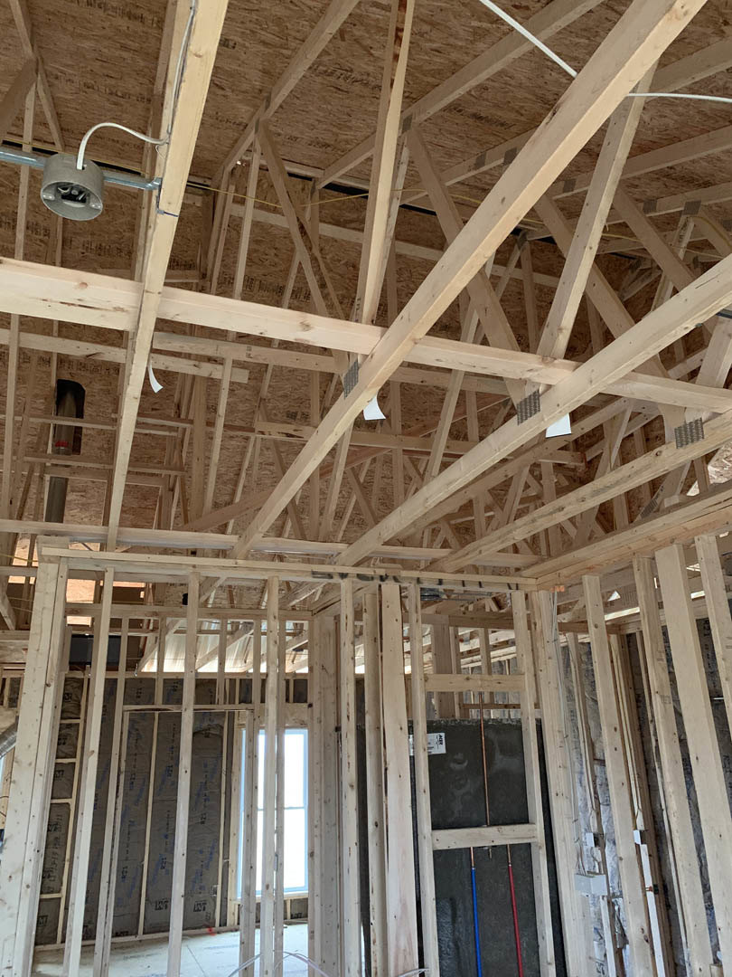 Exposed wood framing and beams with building insulation, steel rods in window opening, white-framed window, and ceiling structure in progress