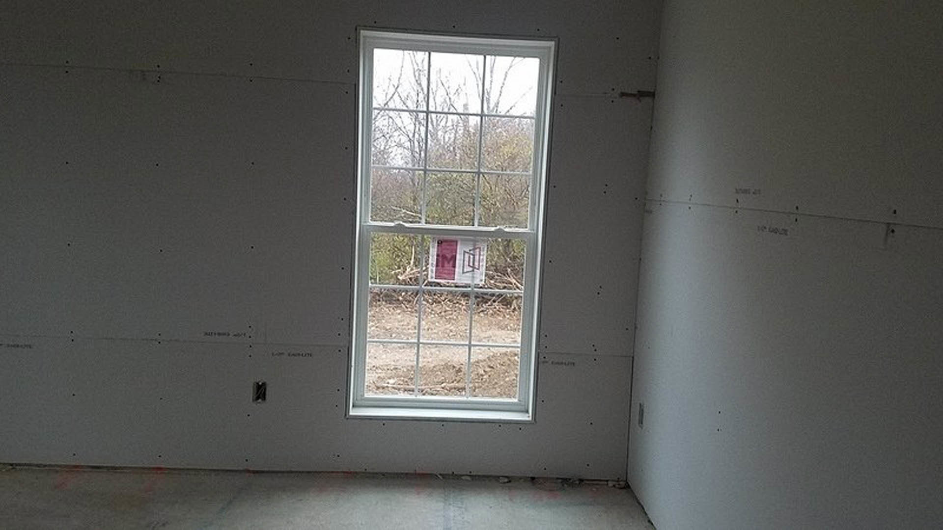 Large window set in a plaster wall, daylight streaming into an empty room with neutral finishes and visible door frame.
