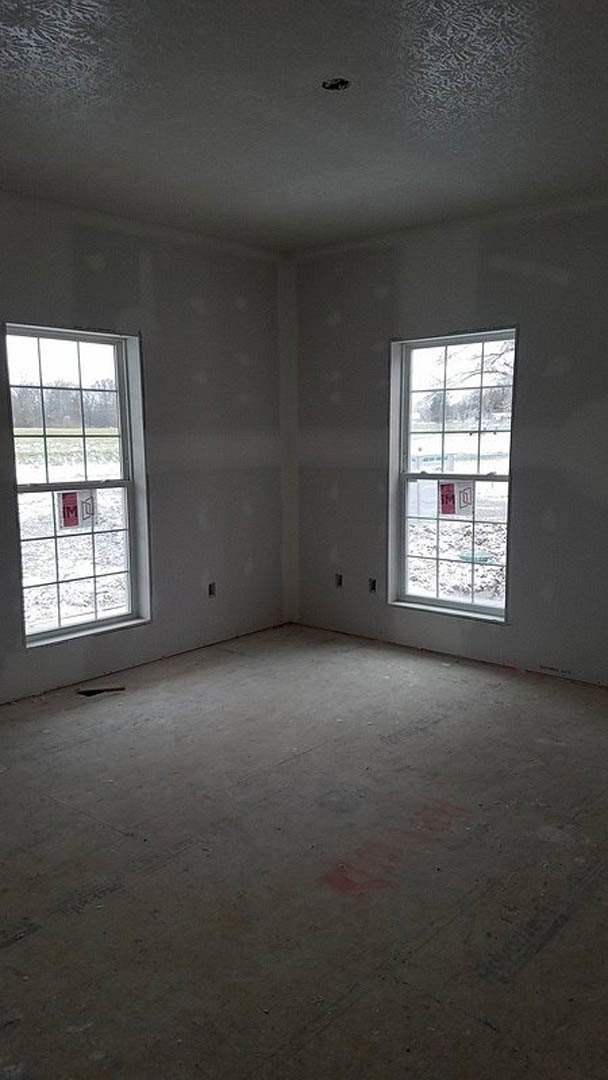 Spacious room featuring large windows, smooth concrete floor, white plaster walls, and a window with a sign; daylight streams in, highlighting a red spot and faint tire print on