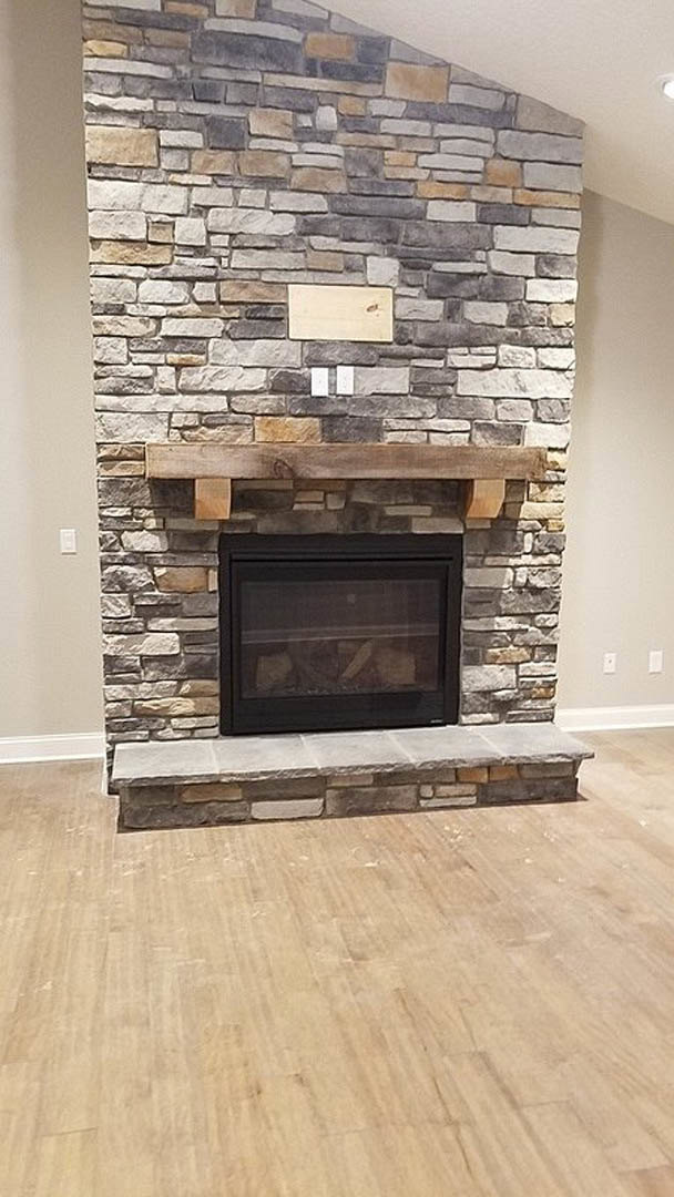 Stone fireplace with wood mantel shelf, wood flooring, and fire screen in a cozy indoor living space