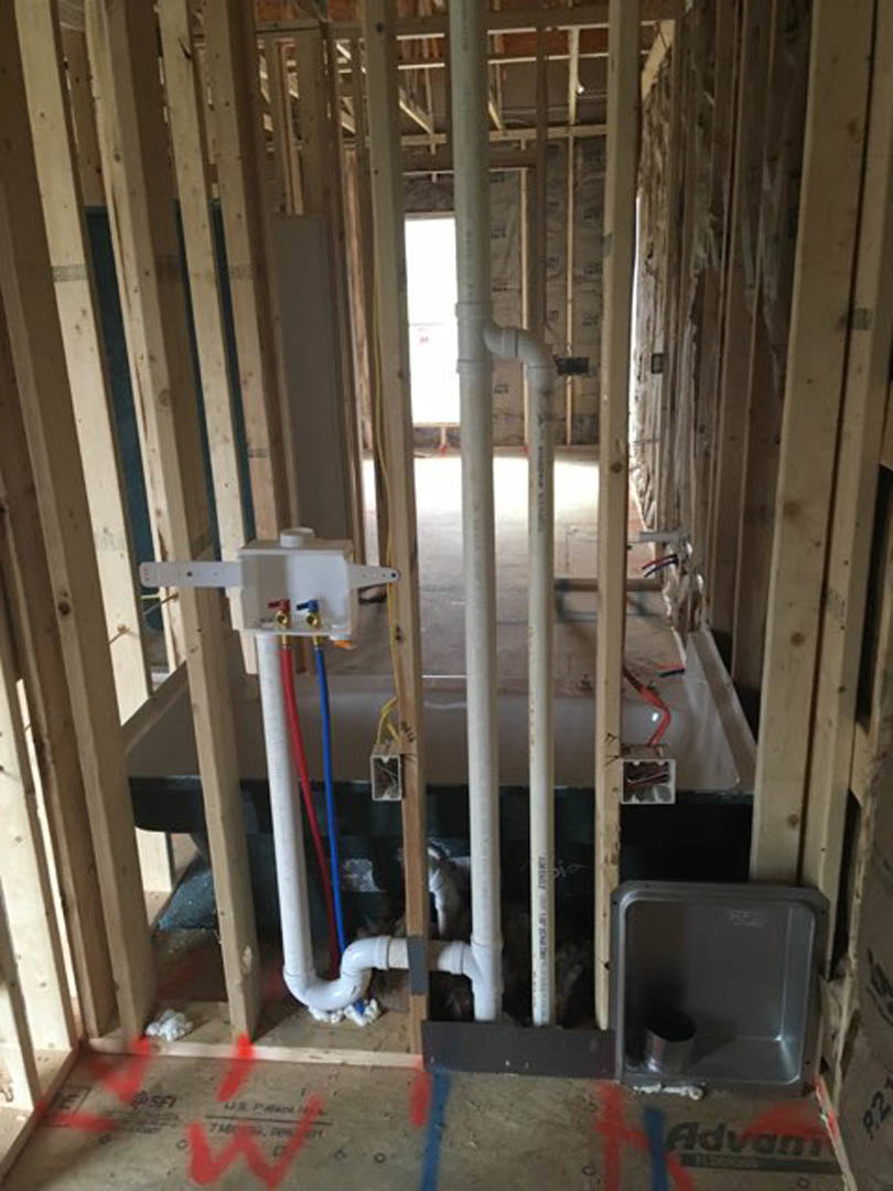 Bathroom under construction with exposed plumbing, unfinished walls, freestanding tub, visible pipes, wood framing, and construction materials scattered on subfloor