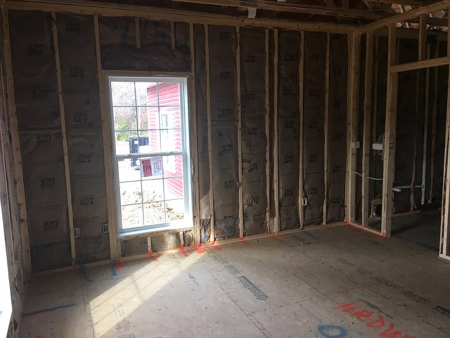 Room with wood-framed window, exposed wood beams, and partially finished walls with visible insulation.