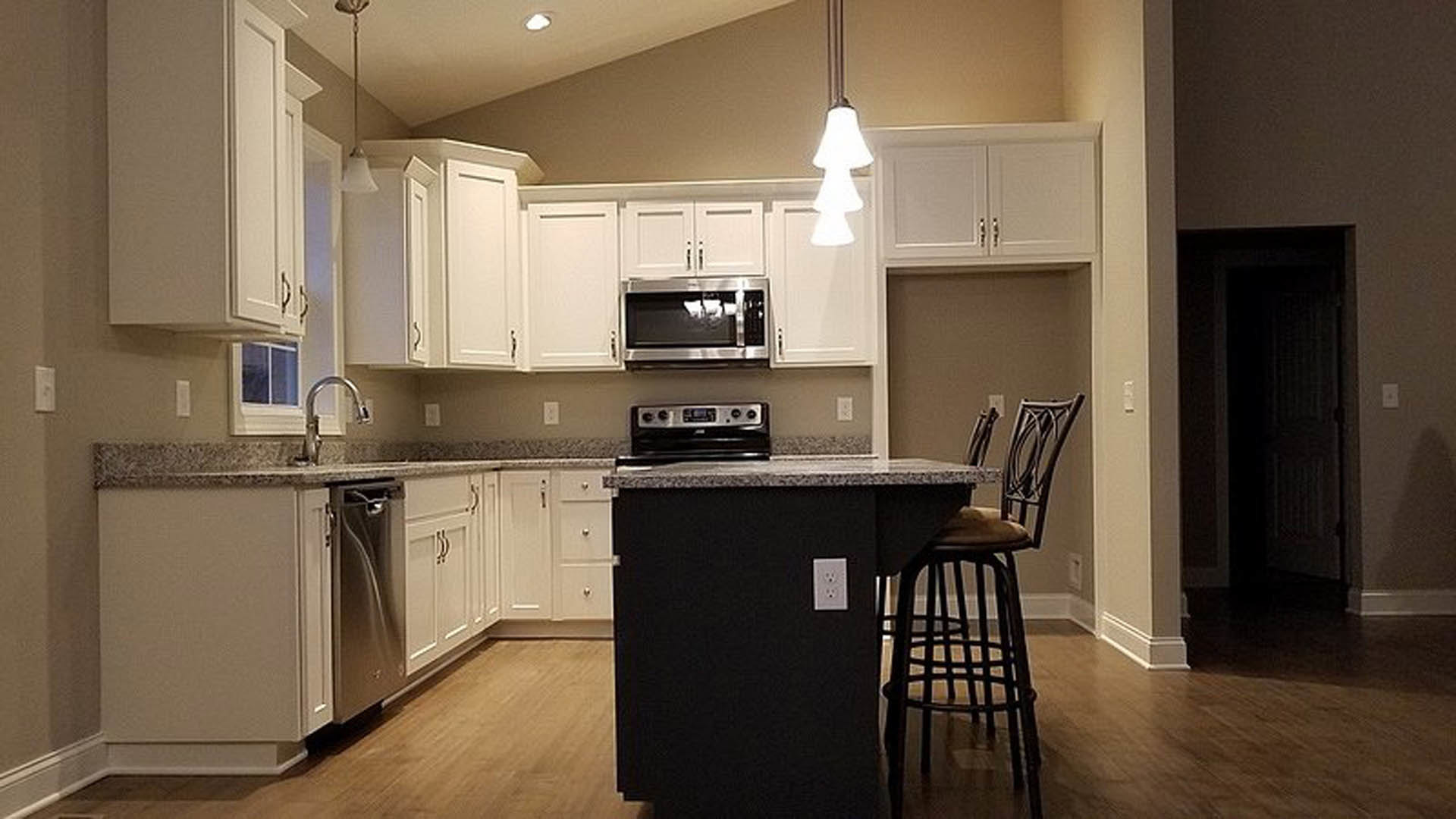 White shaker cabinets, black island with waterfall countertop, stainless steel microwave, bar stools, light wood flooring, modern kitchen appliances
