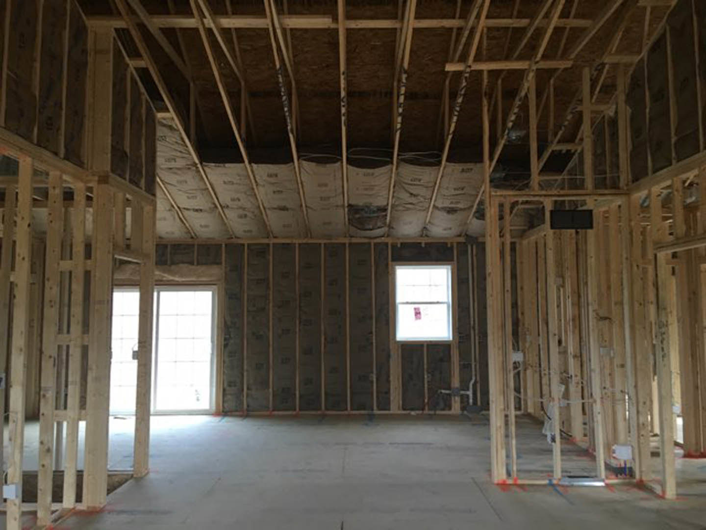 Concrete floor with exposed wooden ceiling beams, large window set in a white wall, pink sign visible on window glass, black rectangular object mounted nearby