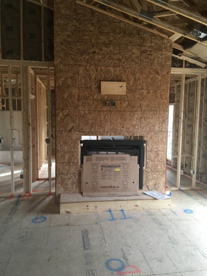 Fireplace surrounded by unfinished plaster walls, concrete floor marked with blue writing, wood paneled wall with sign, construction materials scattered, paper with text, blurry