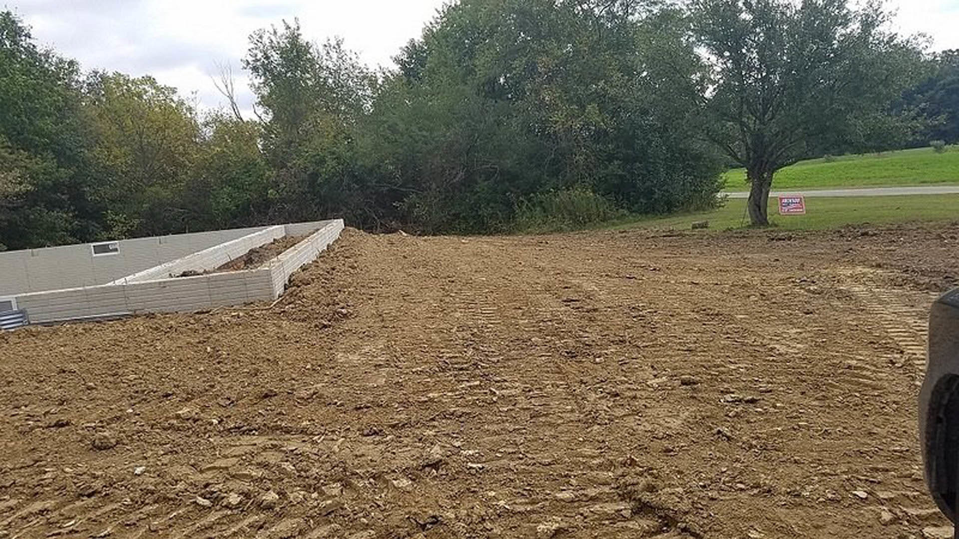 Dirt field bordered by trees and patches of grass under open sky