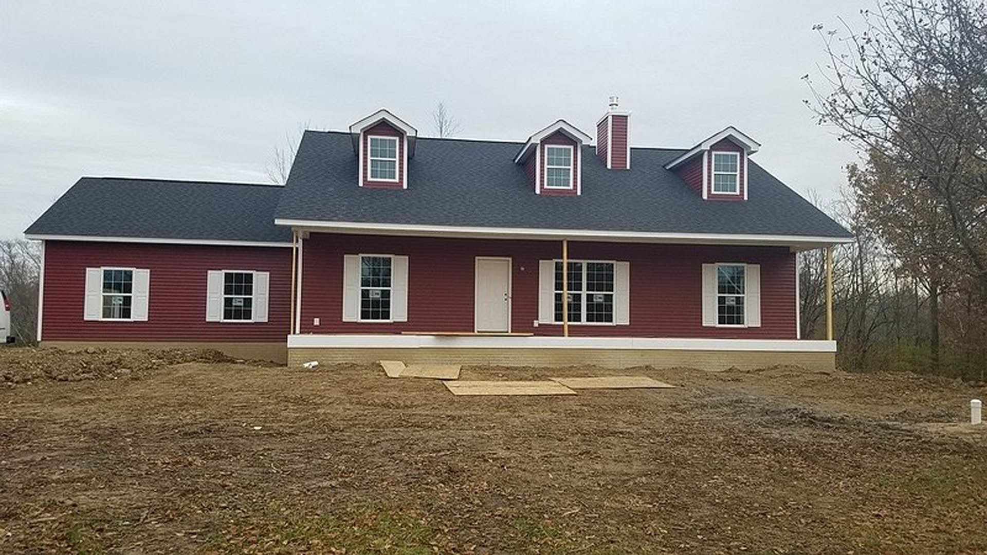 Partially built house with exposed framing, unfinished siding, visible windows, and a dirt yard under a clear sky