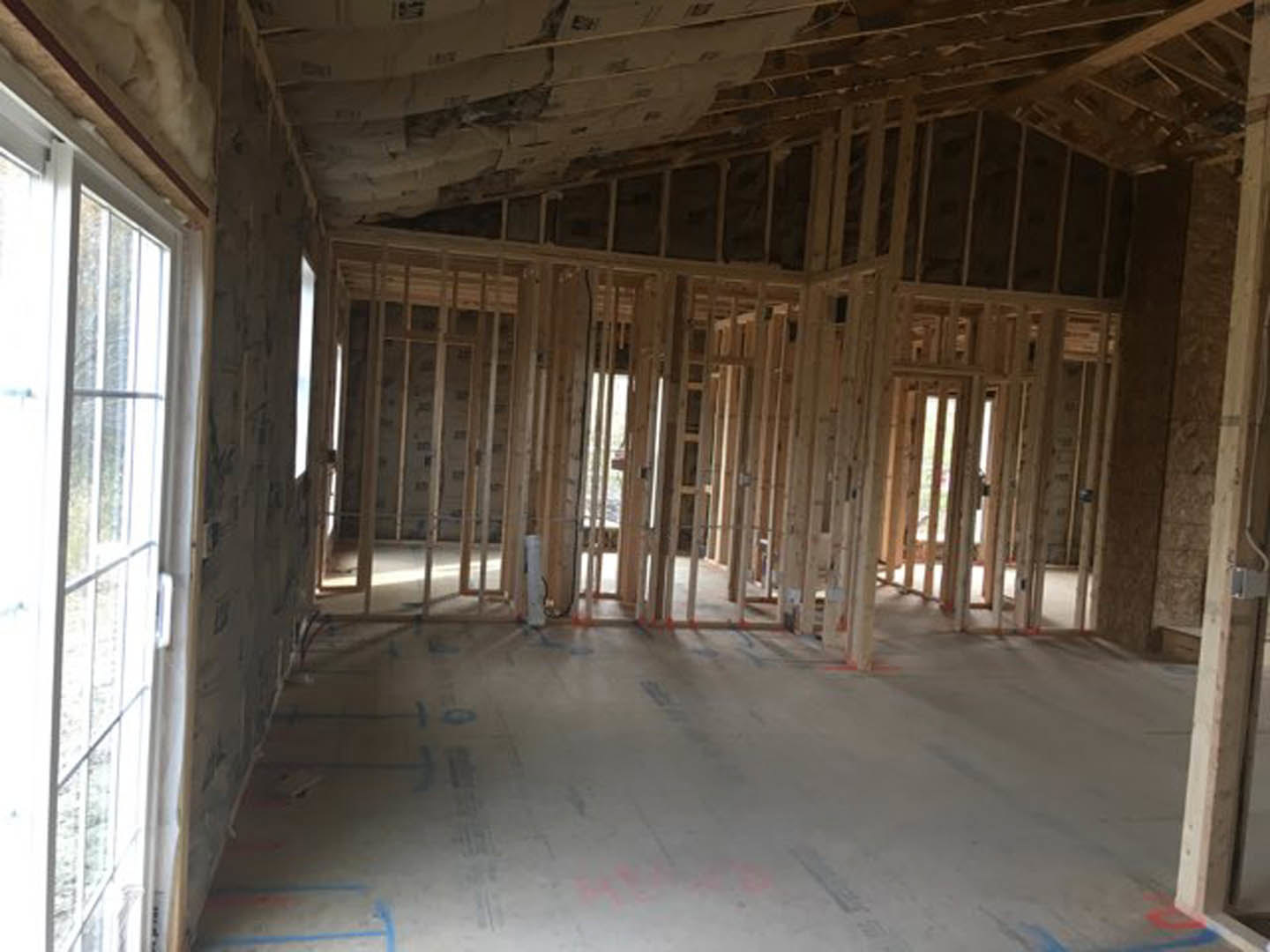 Room under construction with exposed wood framing, unfinished floor with wood beams, window set in wood frame, damaged ceiling, and construction materials scattered on floor