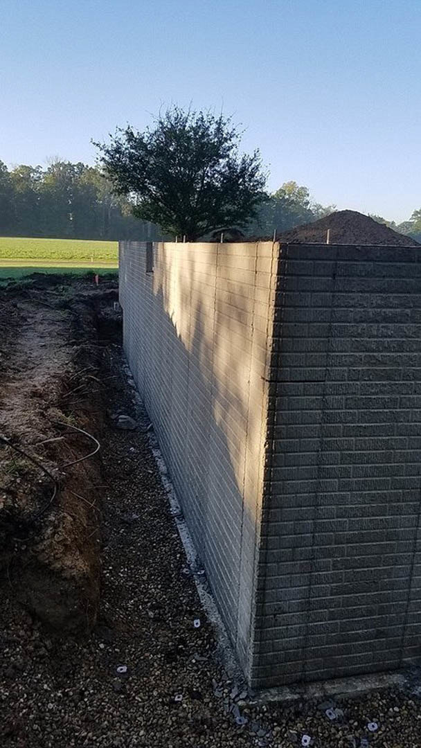 Red brick wall corner with exposed dirt pile in foreground, leafy tree and open sky in background