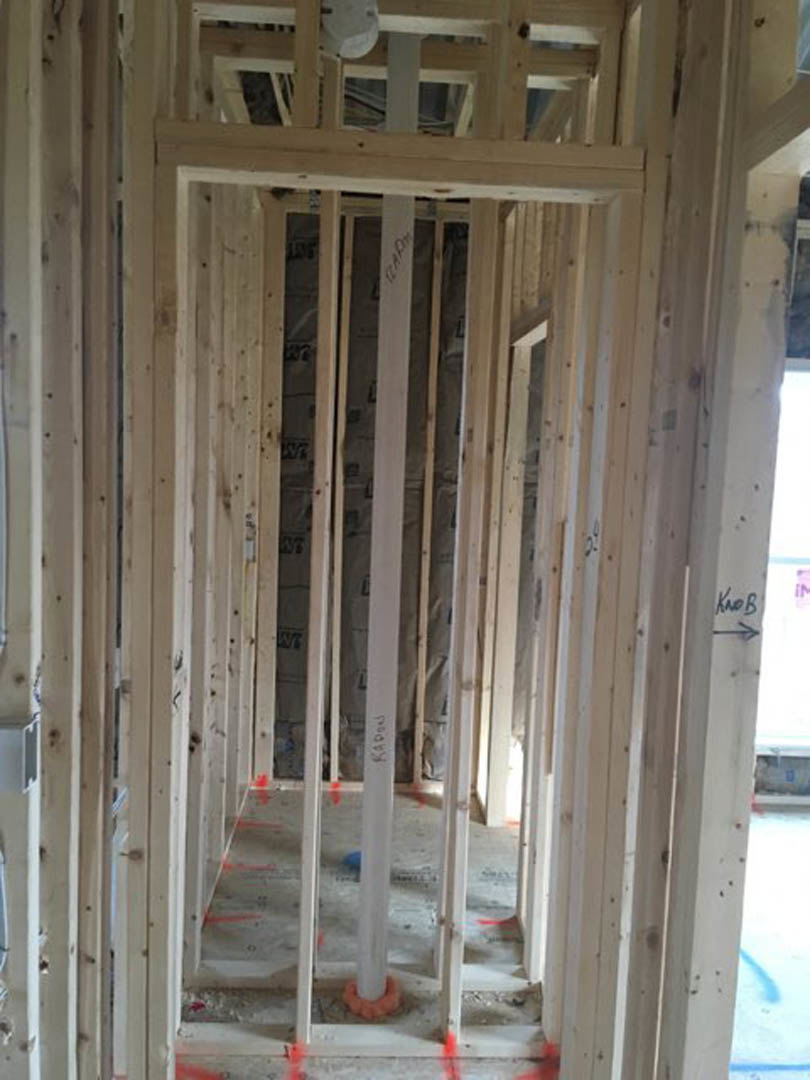 Wood framed walls and ceiling in a partially constructed room, exposed beams and insulation, hand holding a white object near a vertical white pole