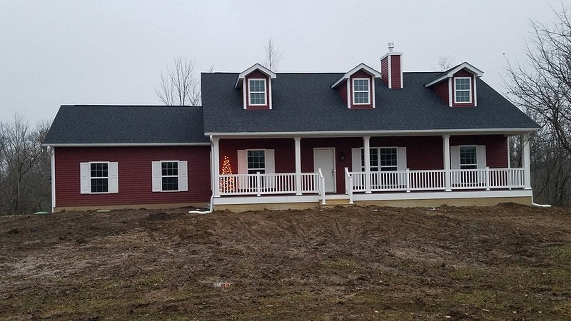 Red roof cottage with white siding, porch featuring white railing, white-framed window, and tree in foreground.