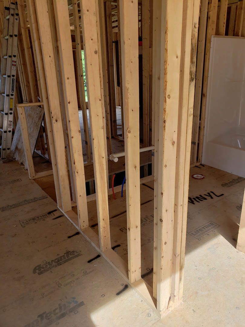 Exposed wood framing and beams with plywood sheathing, white door set in wooden frame, unfinished interior walls, visible building insulation and plaster.