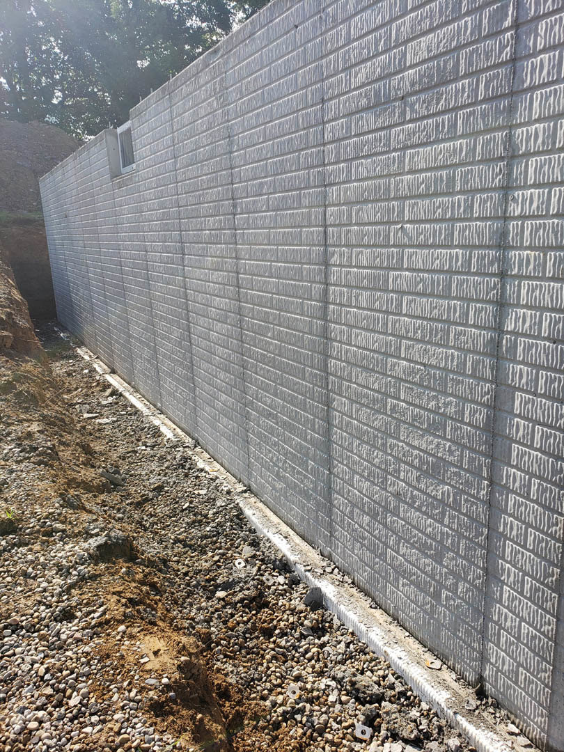 Cement block exterior wall with scattered rocks and dirt at the base, tree partially visible beside the building