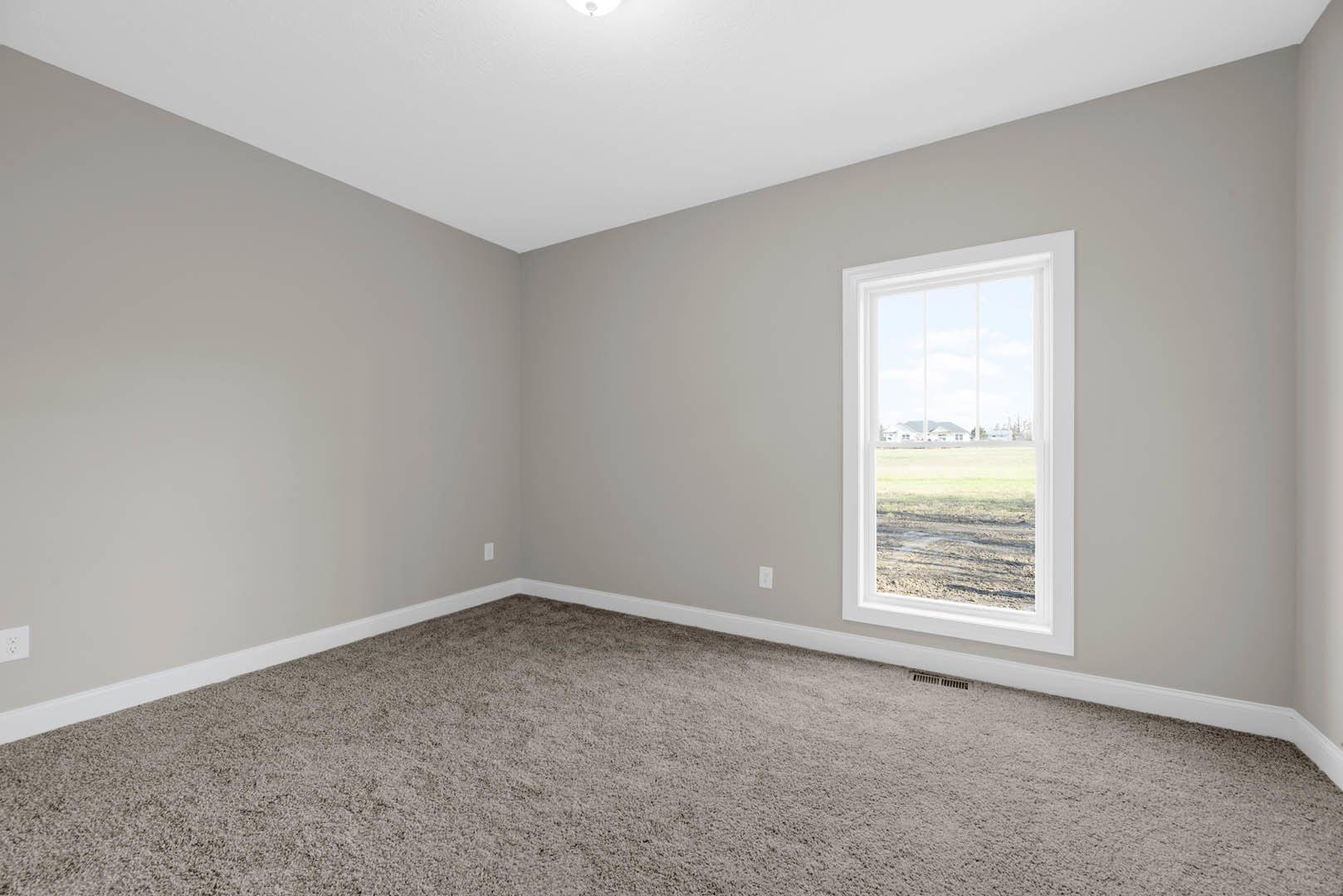 Carpeted room with white walls, large window overlooking grassy field, wood trim along baseboards