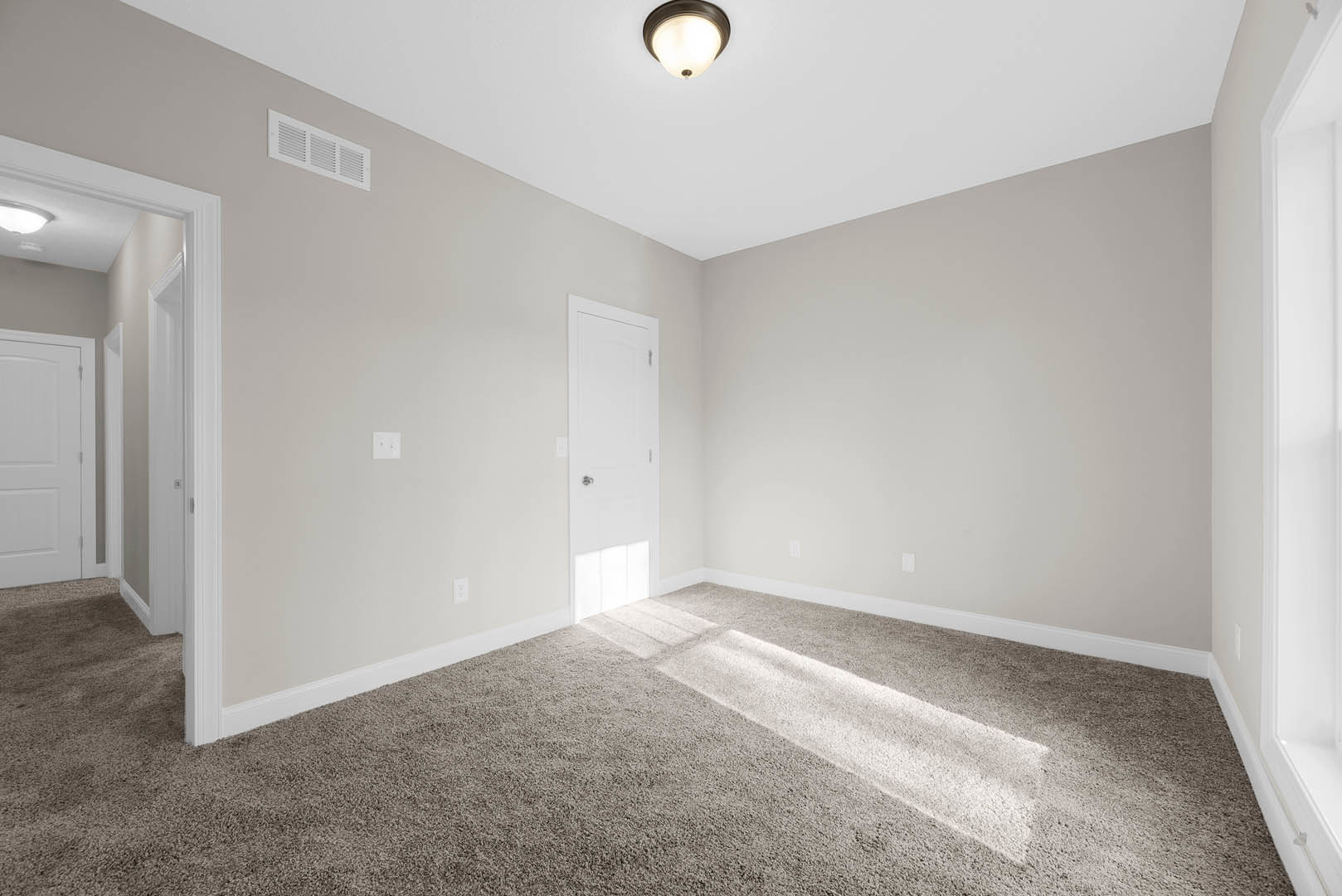Carpeted room with sunlight streaming in, white door featuring a silver handle, ceiling vent, recessed light fixture, white walls with crown molding.