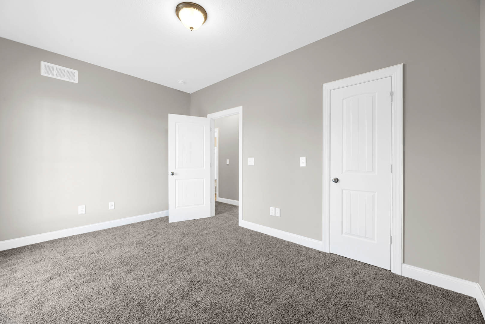 Carpeted room with white doors, silver handles, white trim, ceiling light fixture, and wall vent