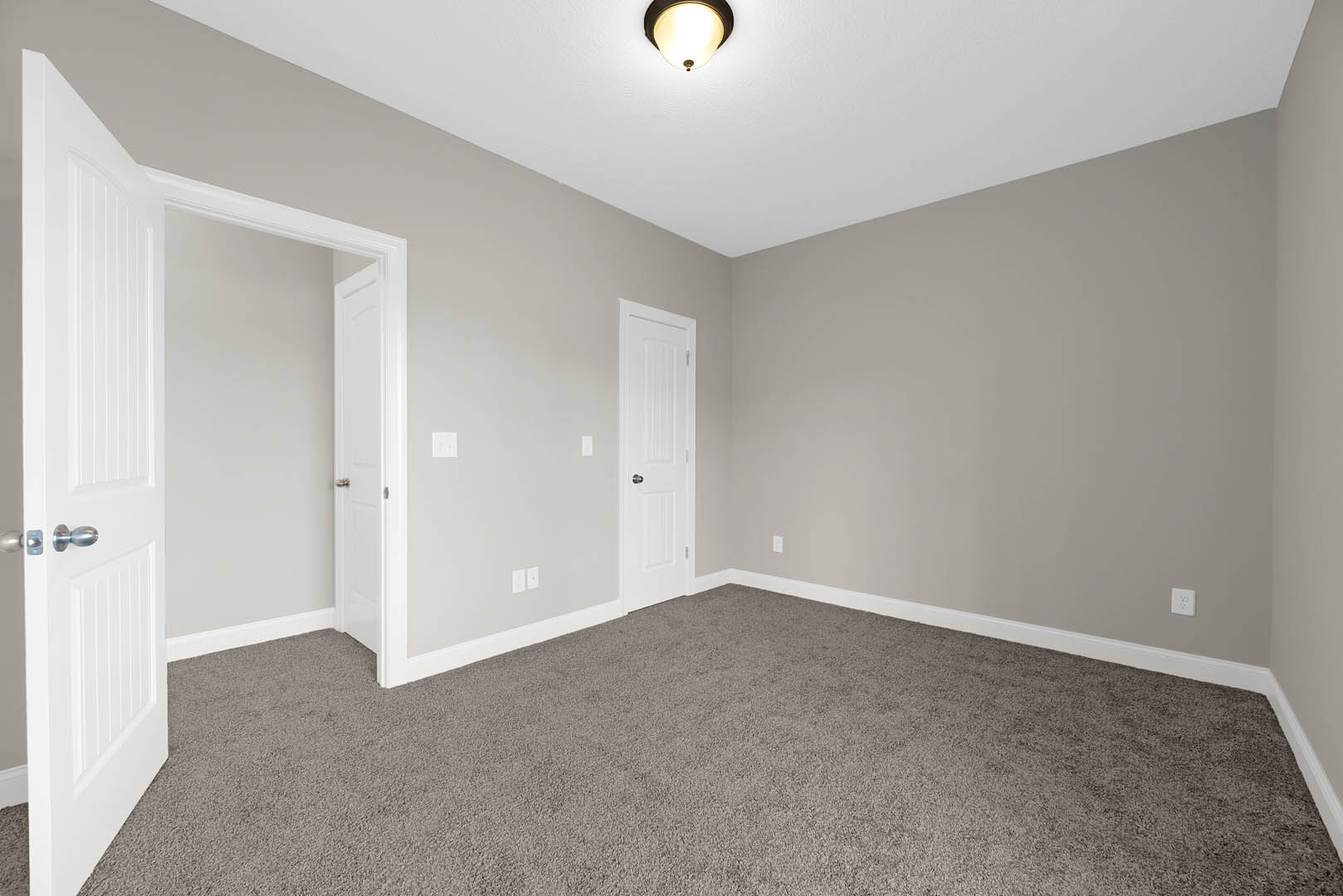 Grey carpeted floor, white walls, white door with silver knob, ceiling light fixture, simple baseboard molding