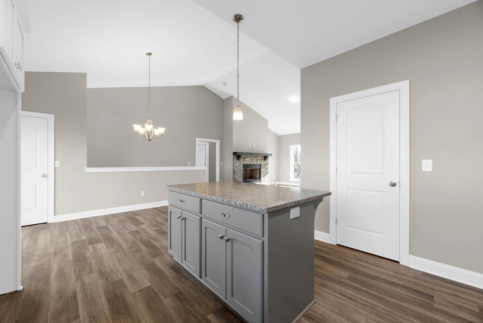 Granite kitchen island with white cabinetry, stainless steel appliances, white door with silver handle, window set in brick wall, hardwood flooring