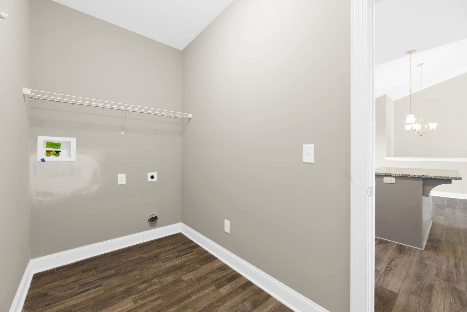 White plaster wall with white baseboards, light wood flooring, white electrical outlet, and a small white box containing green and blue objects; chain detail visible in foreground.