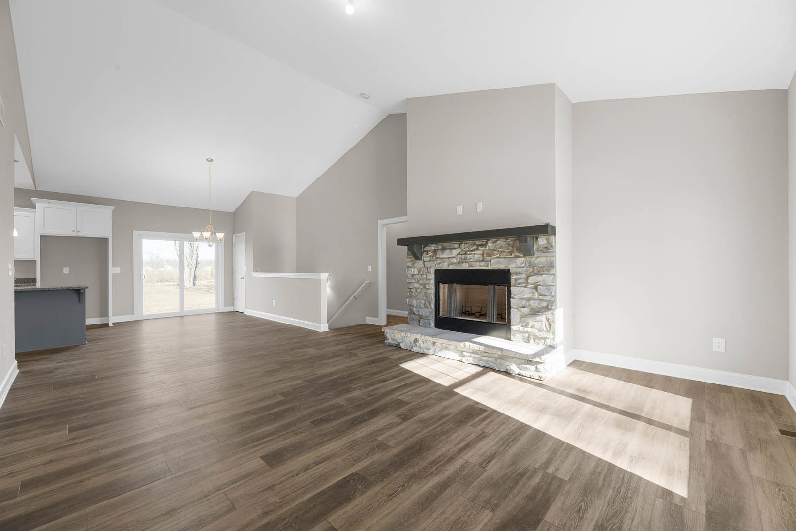 Living room with black glass-door fireplace, wide plank hardwood flooring, marble countertop, large window showing tree outside, plaster walls, and white ceiling.