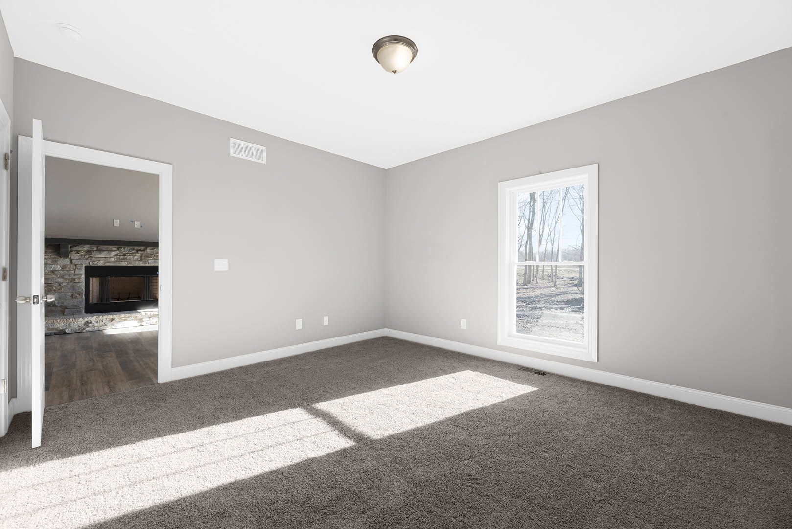 Bright den with laminate flooring, white plaster walls, ceiling vent, recessed lighting, large windows overlooking trees, and a paneled door with decorative molding.