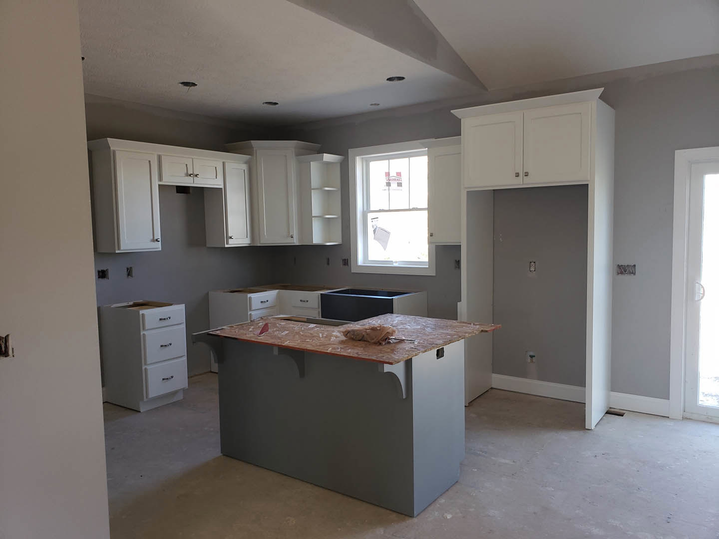 White kitchen cabinets with silver handles, light stone countertop featuring a wooden accent, stainless steel sink, window with a sign, light switch on painted wall, and close-up