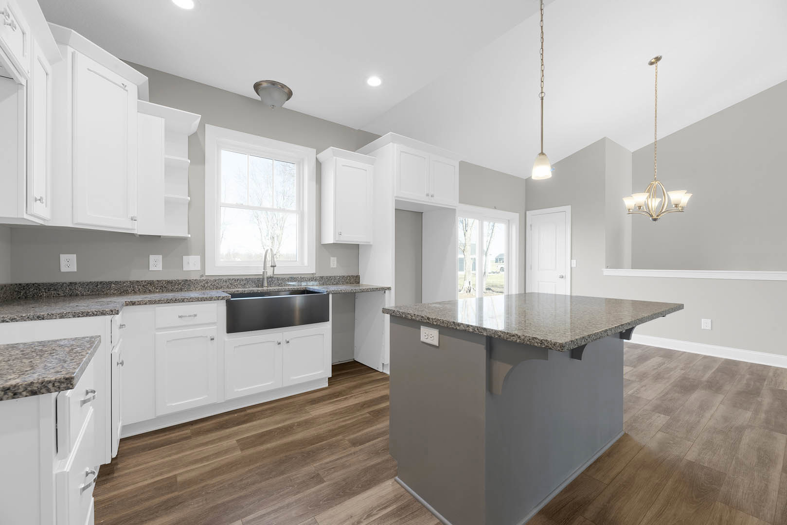 Kitchen with a central island featuring a marble countertop, wood flooring, white-framed window, ceiling light fixture, stainless steel appliances, and white cabinetry.