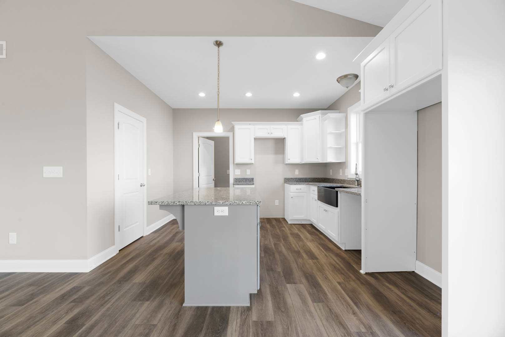 Open kitchen with light wood flooring, white cabinetry, stone countertop, stainless steel sink, modern wall light fixture, and white door with silver handles