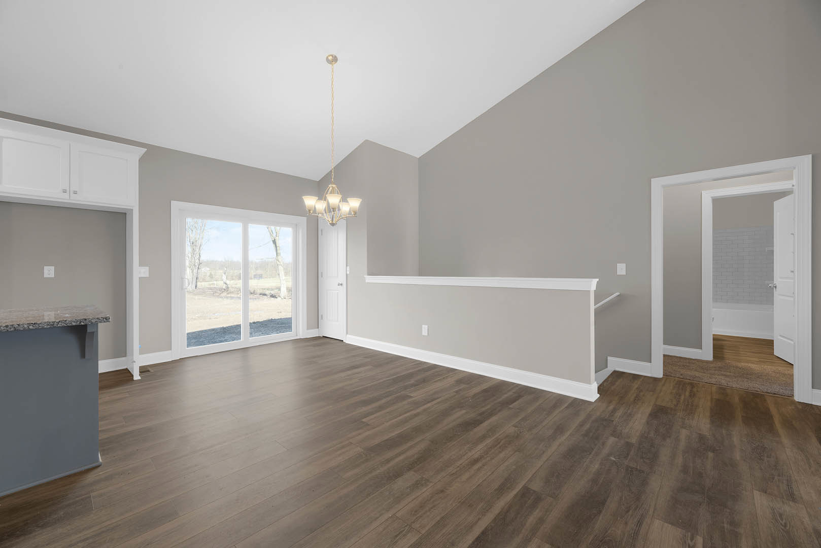 Wood flooring in a room with a white door, white walls, and a window overlooking a grassy field; yellow string hangs from the white ceiling.
