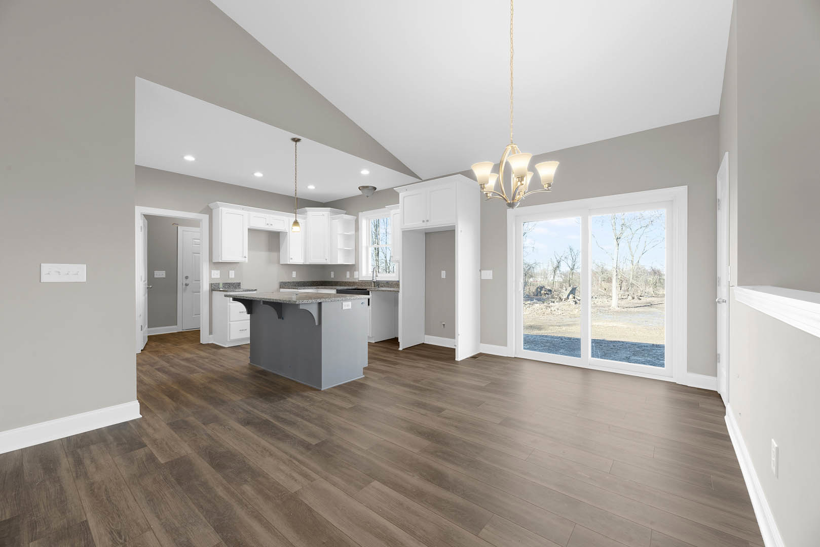 Spacious open-concept kitchen and living area featuring a central kitchen island, hardwood flooring, white cabinetry, glass doors leading outside, and modern light fixtures with