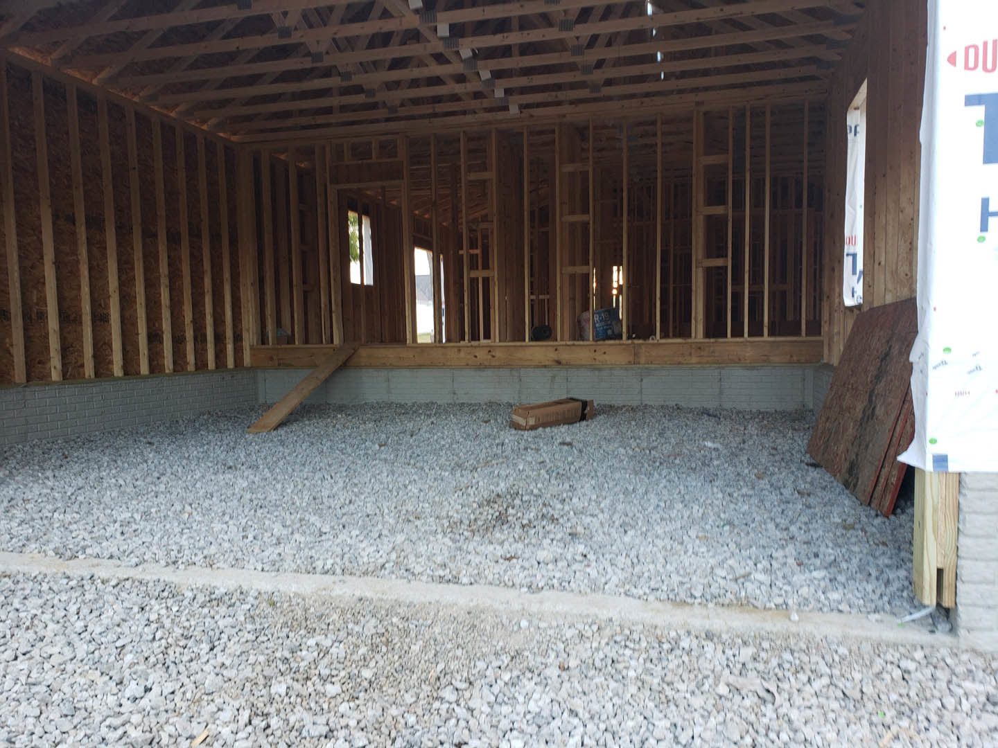Wood-framed room with exposed gravel floor, unfinished ceiling, and scattered boxes on the ground