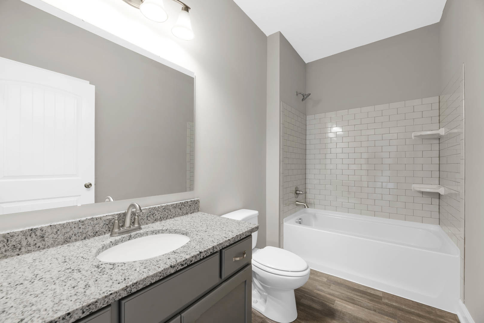 Bathroom with white freestanding tub, wood flooring, white sink with chrome faucet, white door, and tiled walls