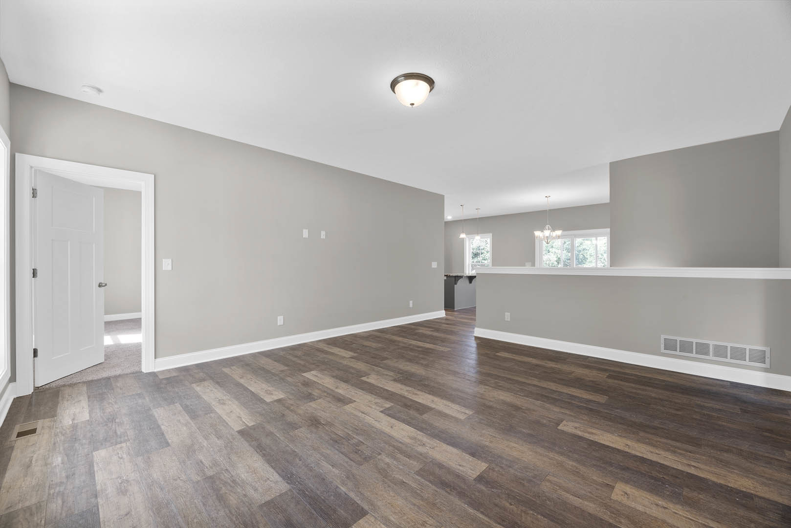 Wood flooring in a room with white walls, white door featuring silver handles, ceiling light fixture, and wall vent