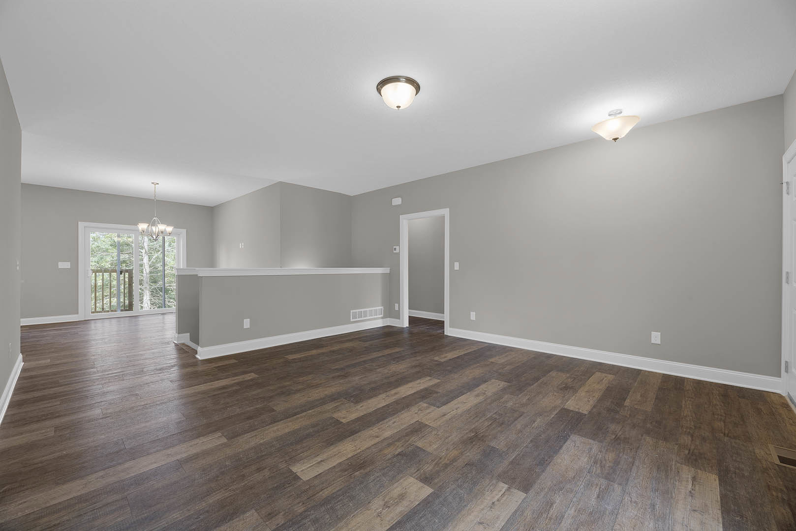 Wood flooring, white walls with white trim, ceiling light fixture, white door with matching frame, window showing trees outside