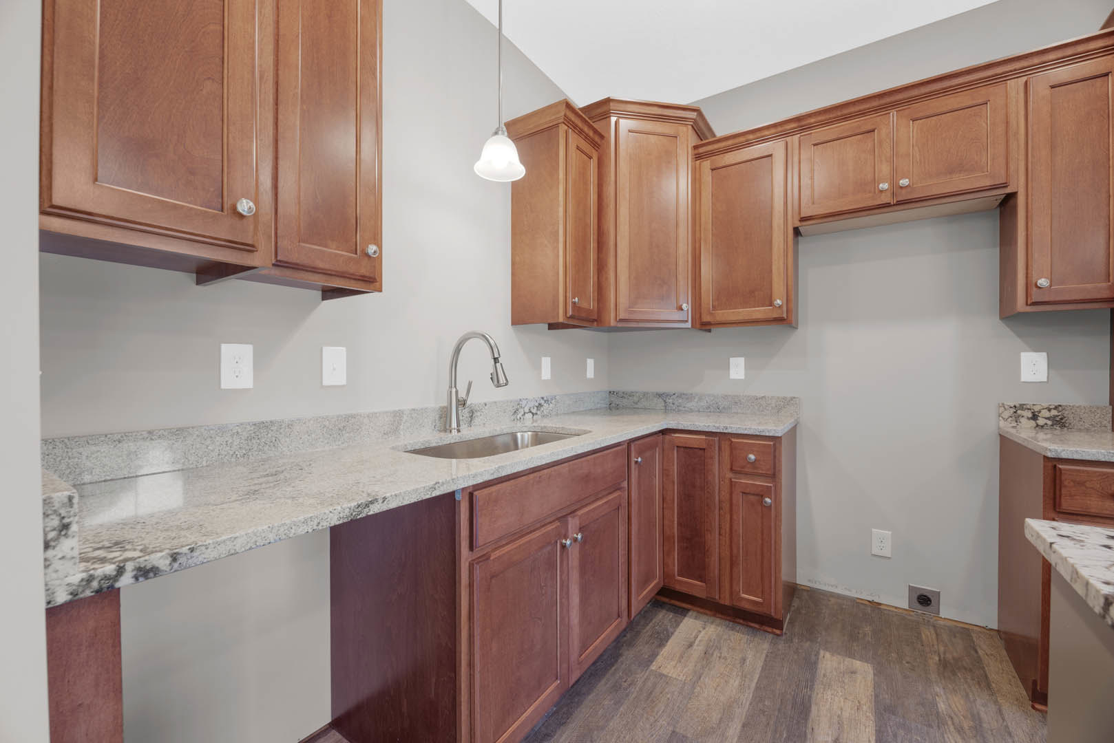Kitchen with natural wood cabinets, granite countertops, stainless steel sink, white walls, hardwood flooring, and modern fixtures including a close-up of a faucet and electrical
