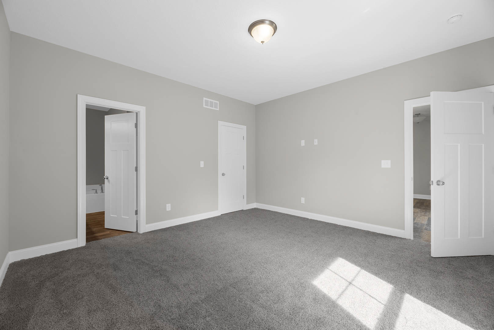 White walls, grey carpet flooring, white door with silver handle, ceiling light fixture, simple molding along baseboards