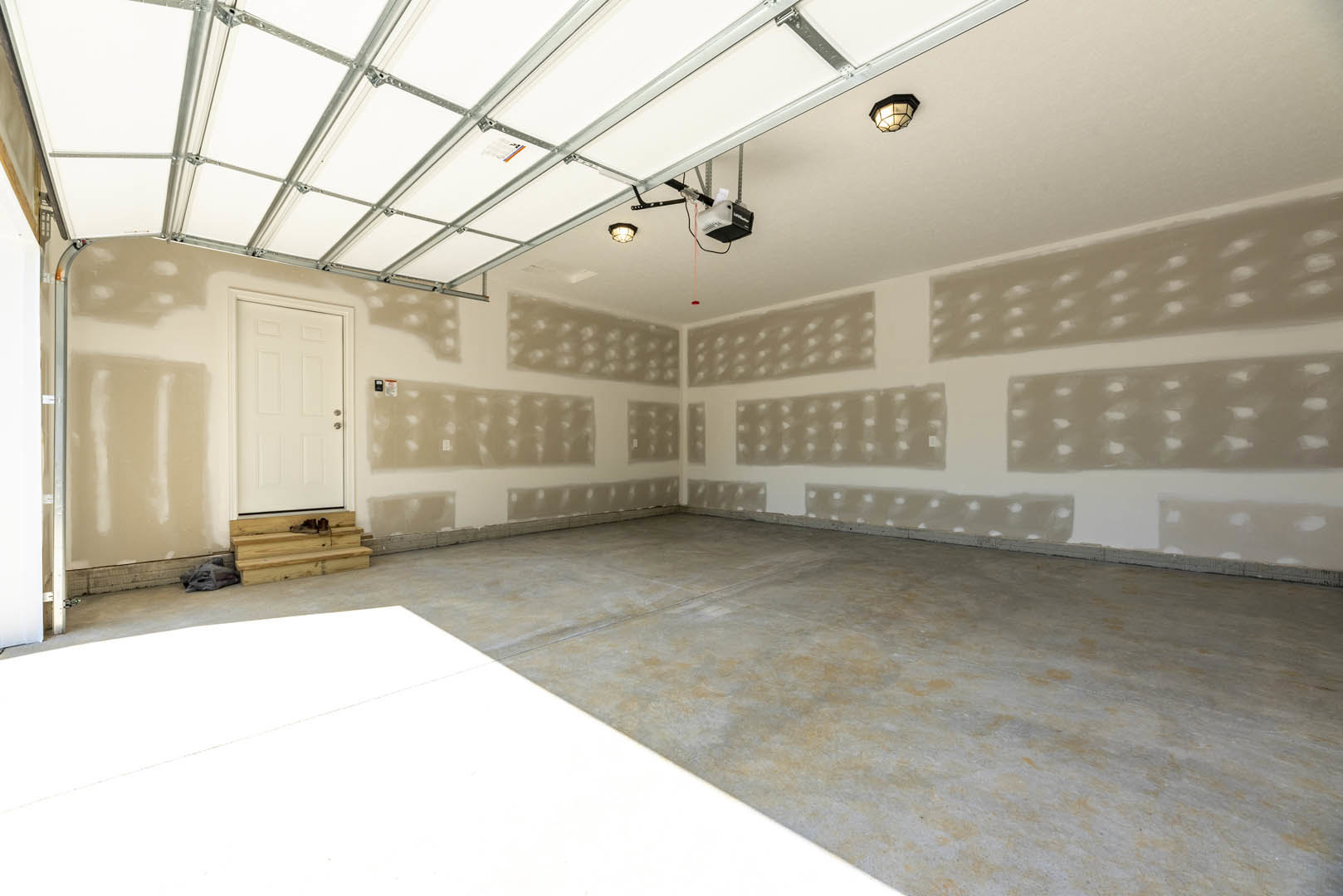 White-painted room with two matching doors featuring silver handles, glass-shaded ceiling light fixture, wood plank with visible bolt, concrete floor, and a blurry cat lying on
