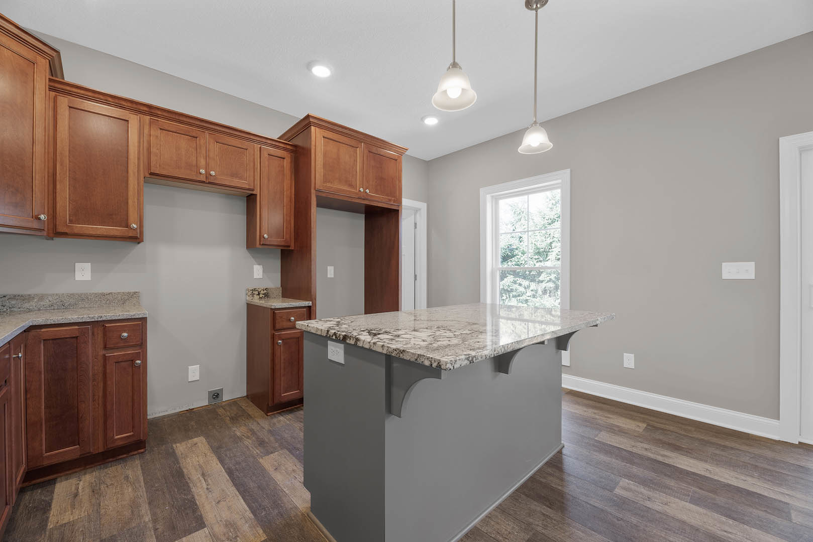 Marble countertop kitchen with wooden cabinets, stainless steel sink, white outlet with three switches, window overlooking snow-covered trees, and pole-mounted light fixture
