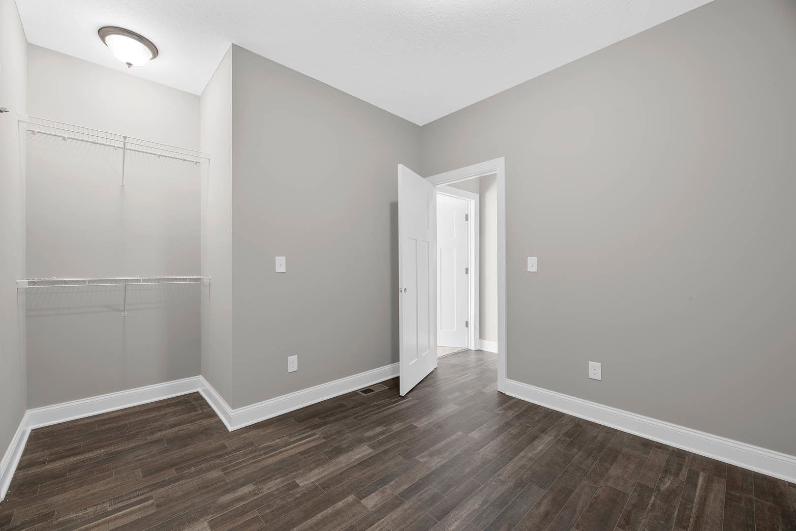 Open white door leading into a room with wood laminate flooring, white walls, and a ceiling-mounted light fixture