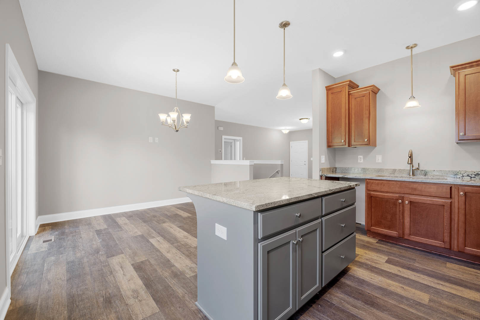 Kitchen with wide-plank wood floors, central island featuring marble countertop, white cabinetry, stainless steel sink, and built-in appliances
