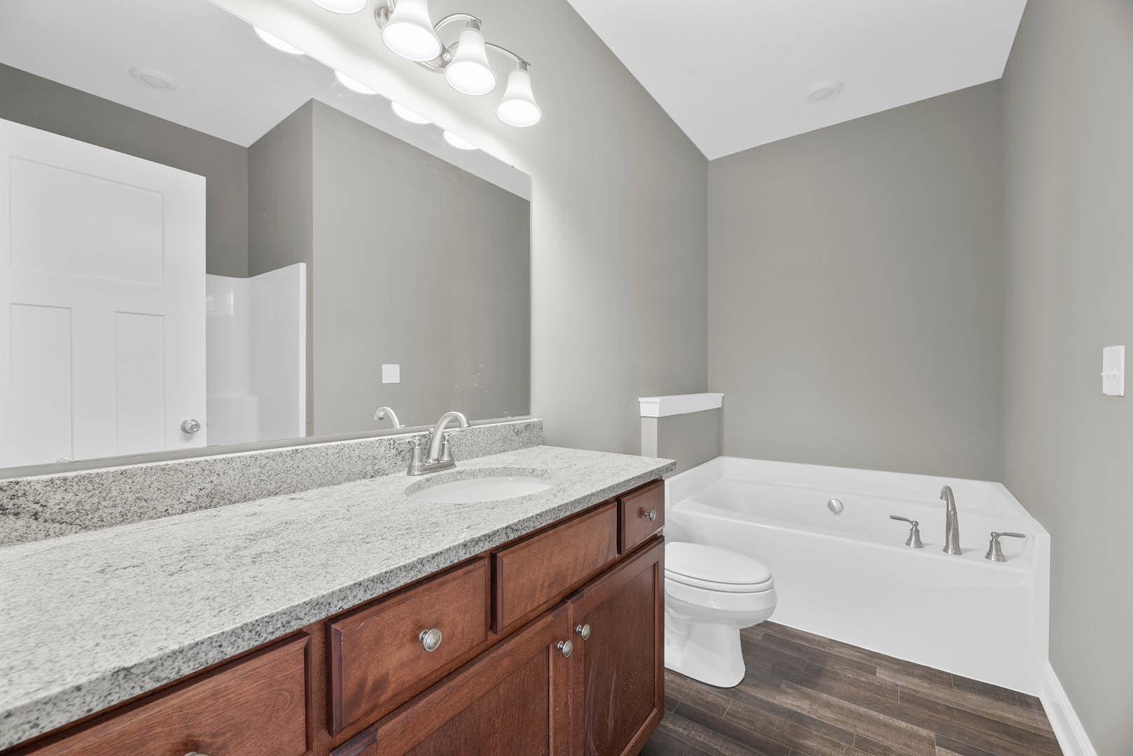 Bathroom featuring a white bathtub with silver faucet, wooden flooring, white toilet, countertop with sink and mirror, and a close-up of a white door